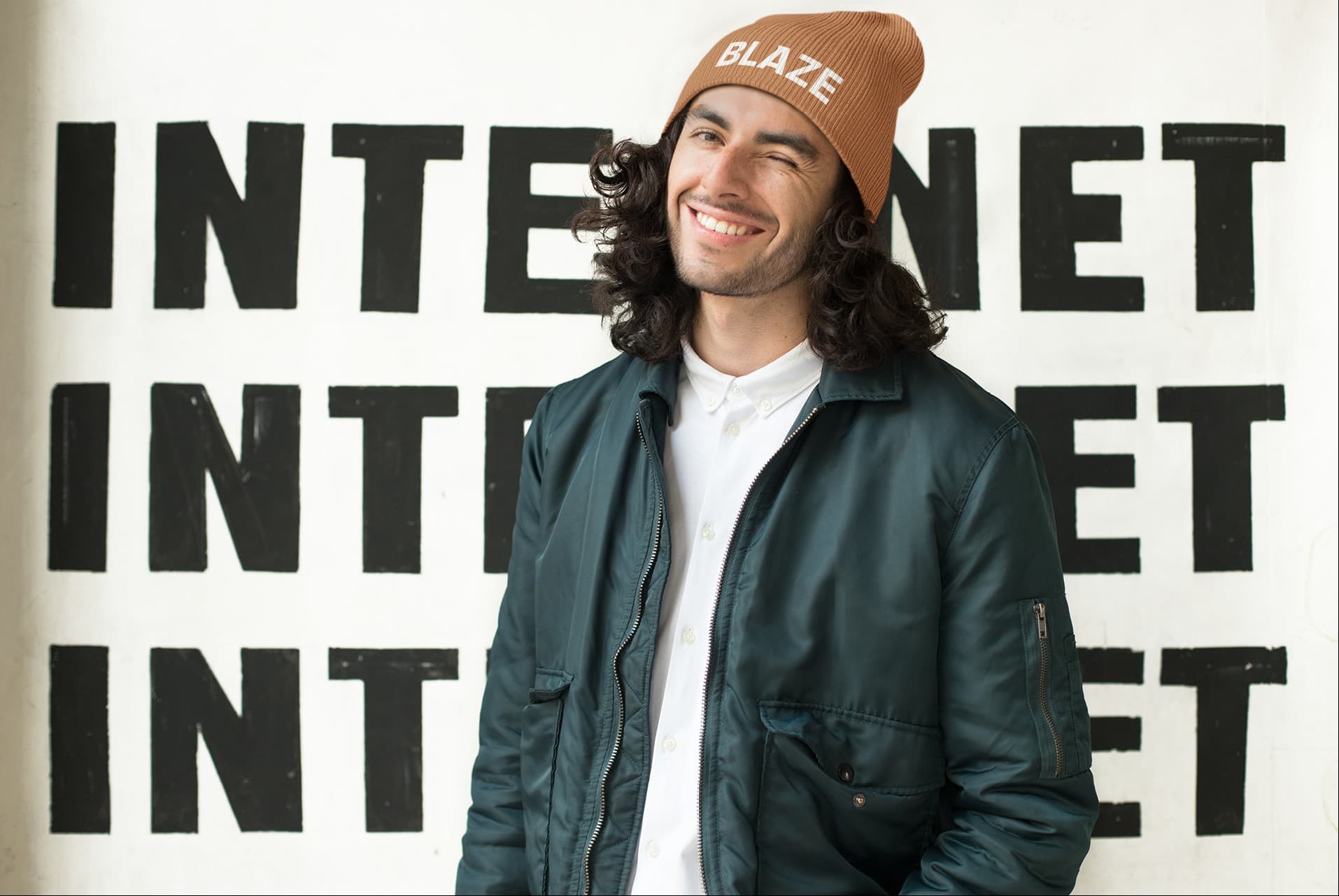 A rust BLAZE beanie worn in front of a painted INTERNET wall.